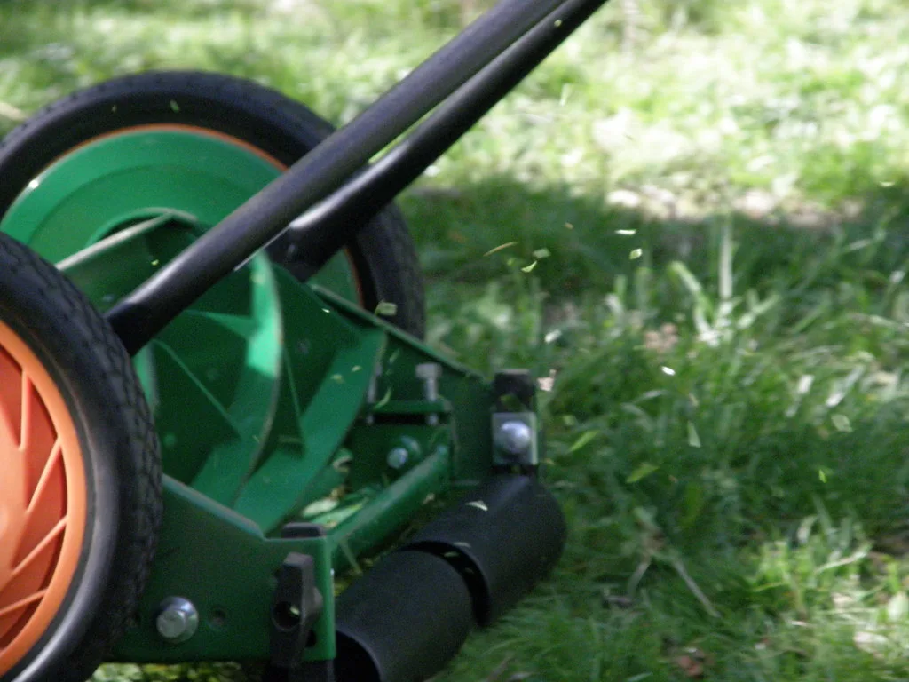 Une tondeuse manuelle hélicoïdale verte posée dans l’herbe